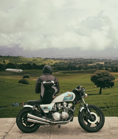 男子坐在摩托车上,面对广阔的绿地
